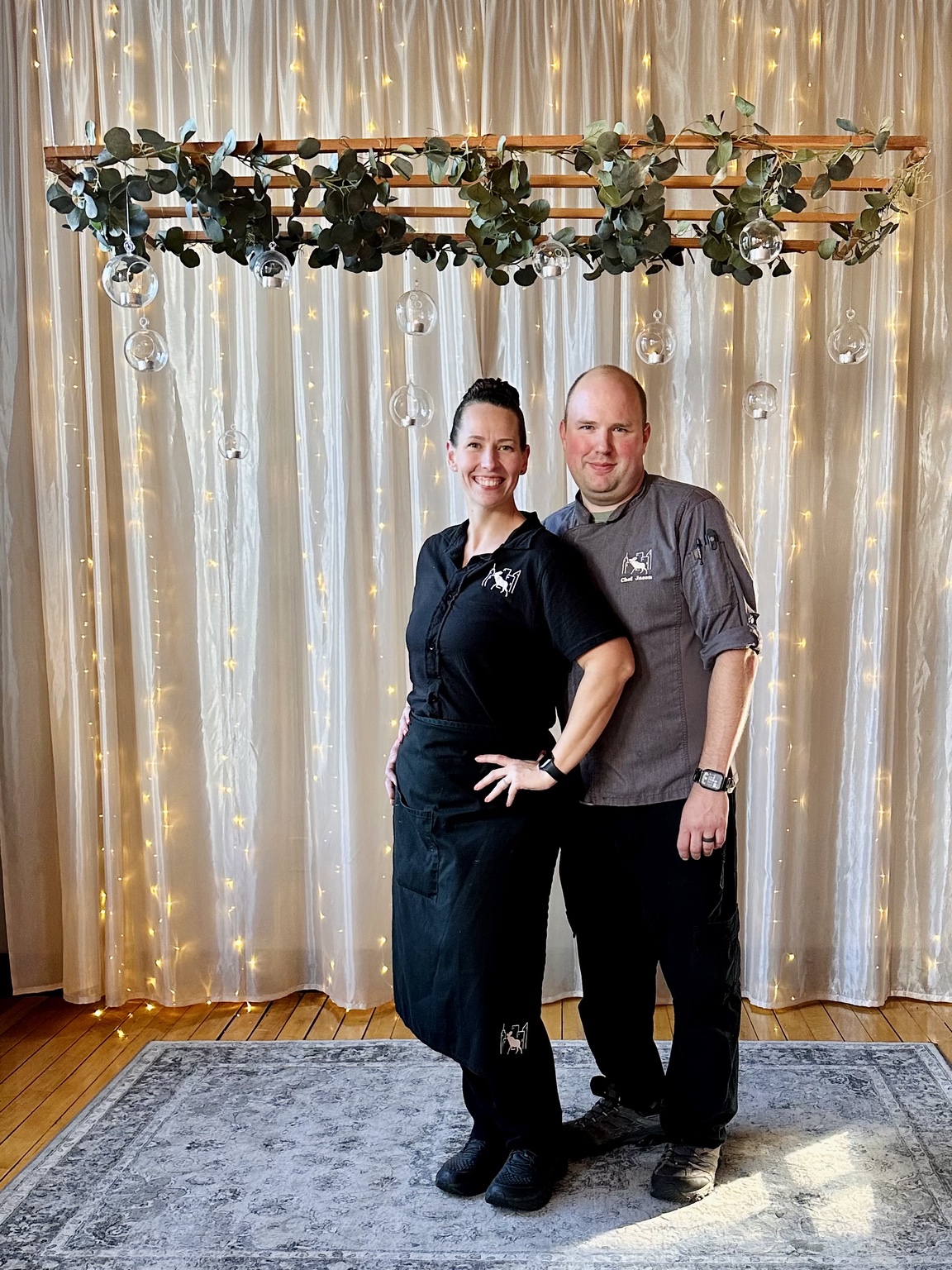 Stacy and Chef Jason standing together in front of greenery and string lights